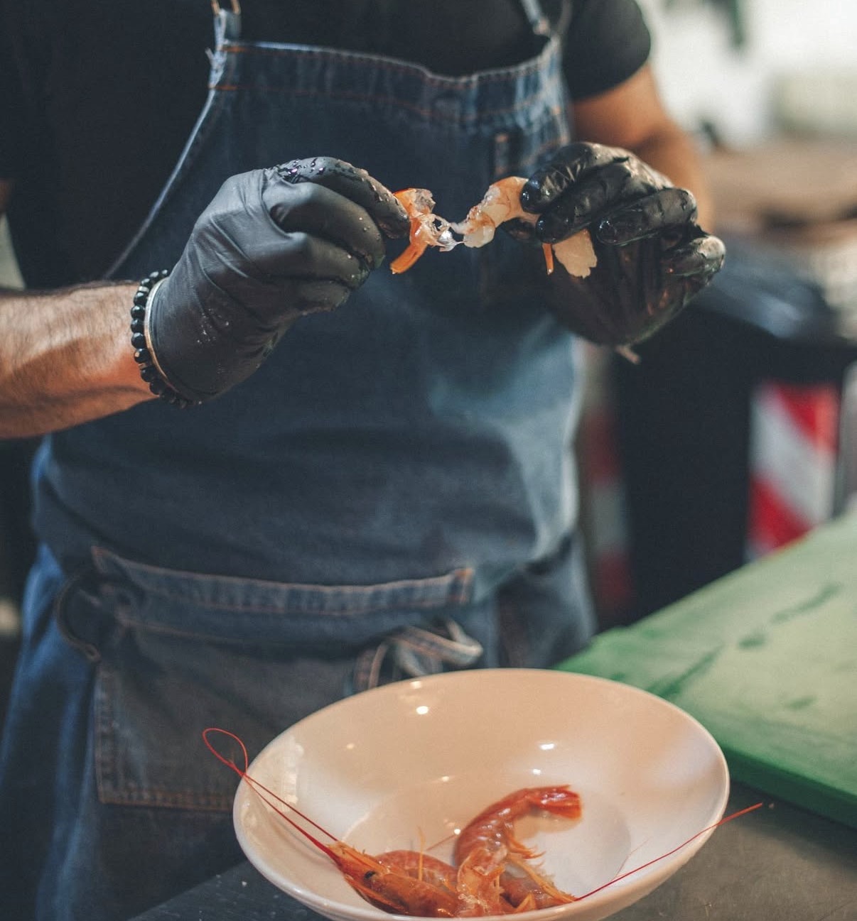 Cuoco con grembiule in denim e guanti neri che pulisce un crostaceo sopra un piatto