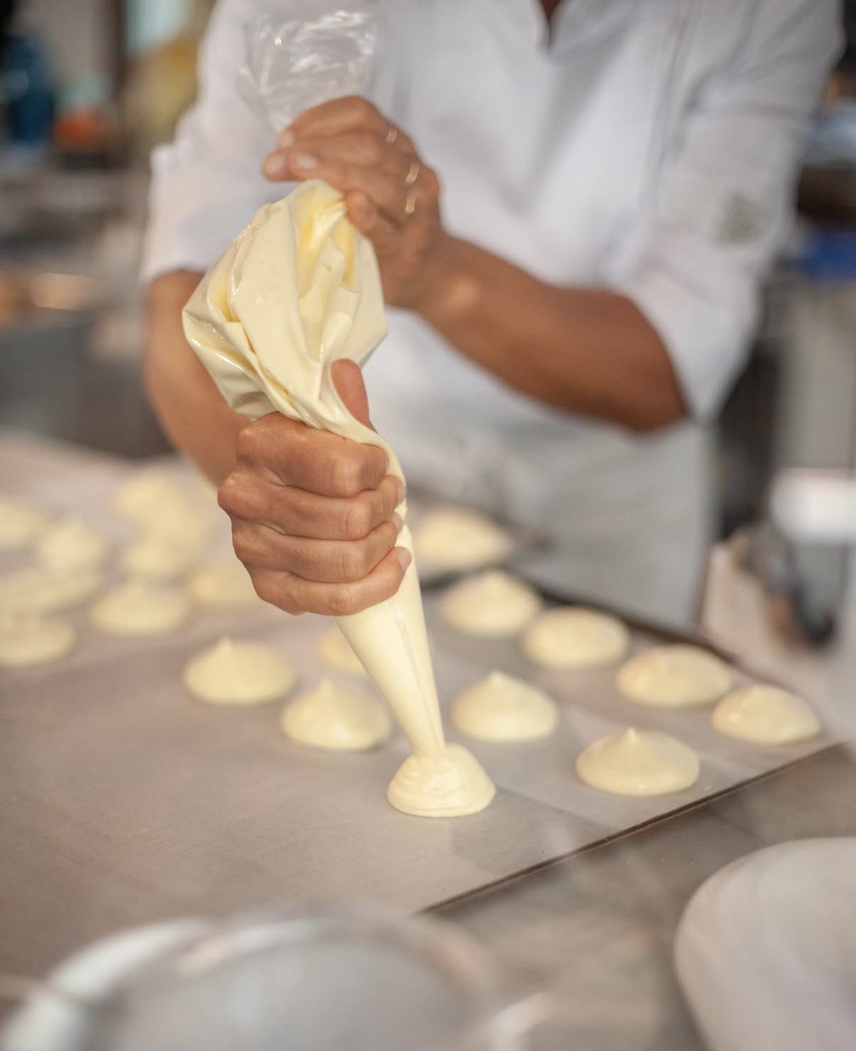 Una mano dosa con la sac à poche piccoli ciuffi di composto su una teglia