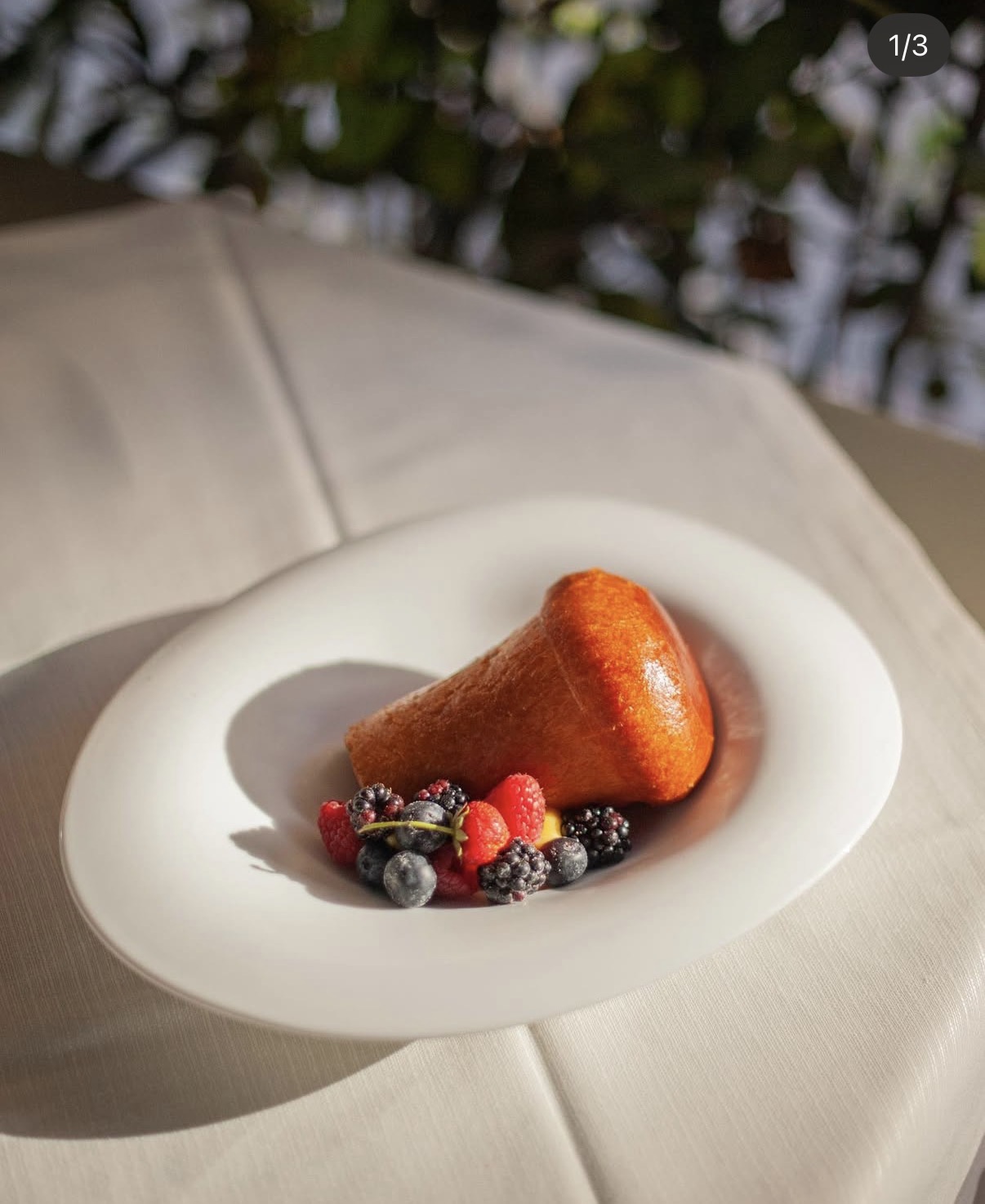 Babà su piatto bianco con frutti di bosco freschi, in una composizione luminosa su tovaglia chiara